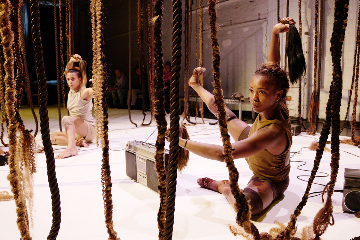The two performers perform on the floor between lianas and hold hair in their hands