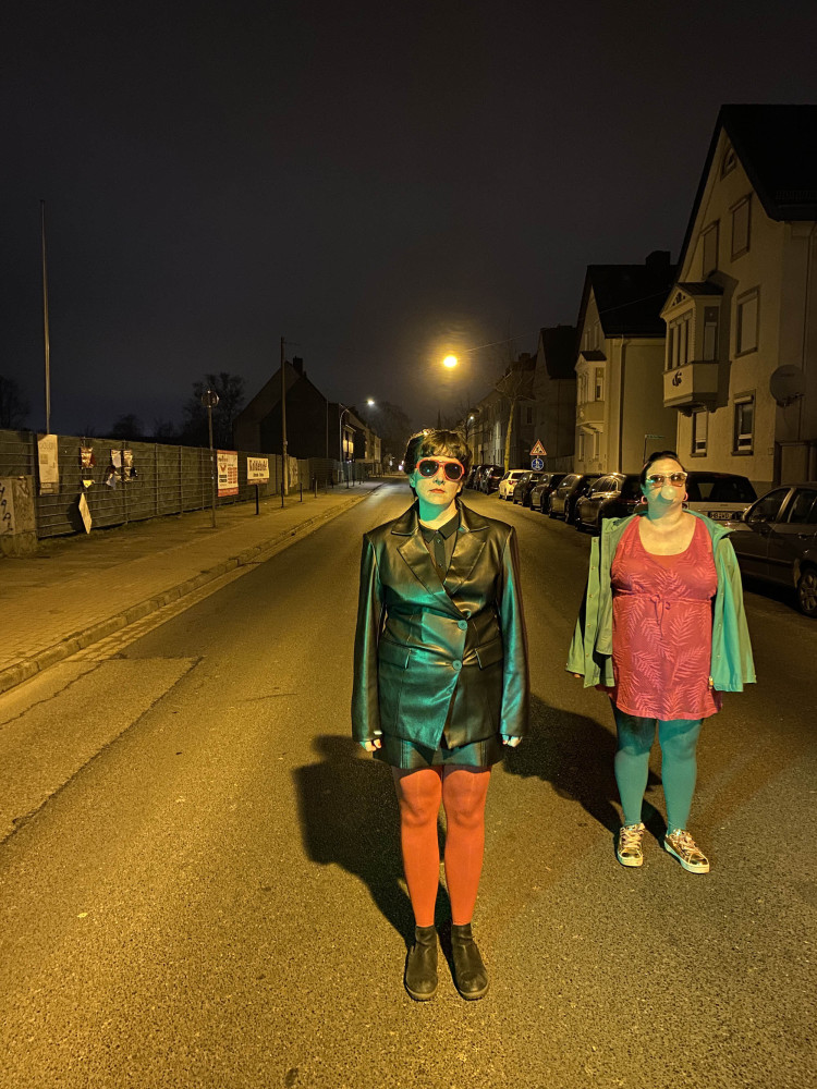 Zwei Personen stehen auf der Straße. Es ist Nacht.